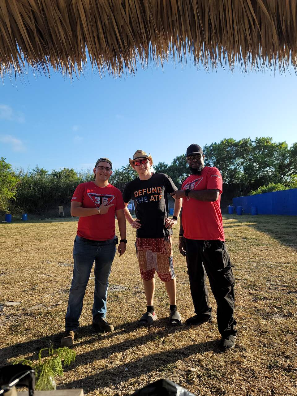 Three men smiling and posing at the outdoor range during a training session at 3B Tactical in Miami, FL