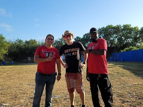 Three men smiling and posing at the outdoor range during a training session at 3B Tactical in Miami, FL